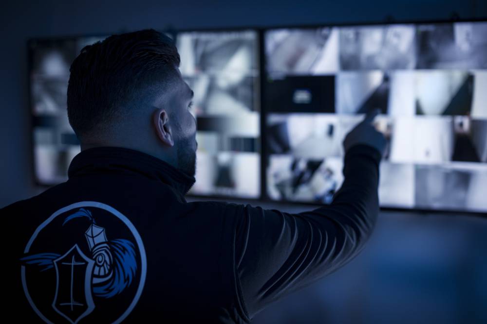 Sicherheitskraft zeigt auf einen Bildschirm mit Aussschnitten der Videoüberwachungskameras im Objekt